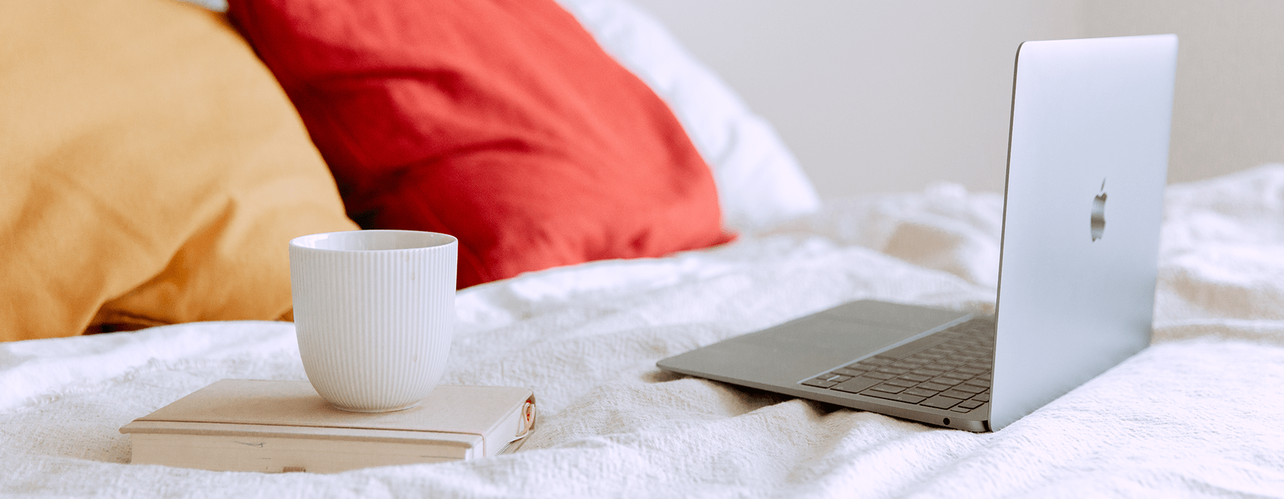 lifestyle image of a bed with a laptop and a cup of coffee on the bed
